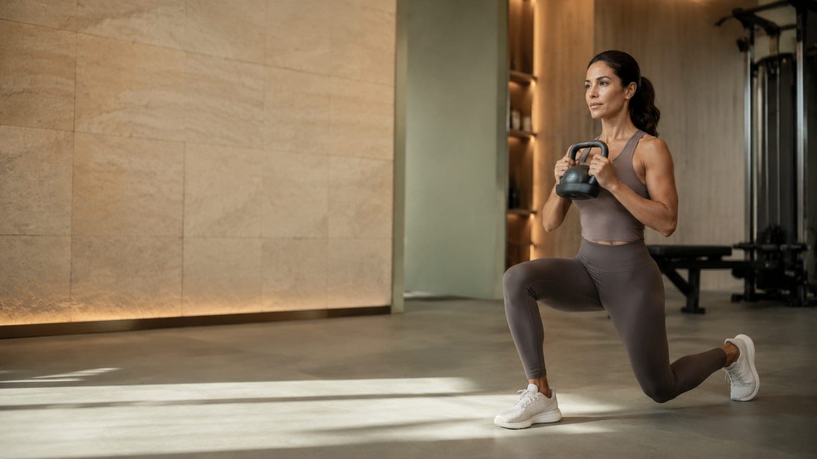 Mujer entrenando con kettlebell frente a un muro de piedra cálida en FITNATIONS